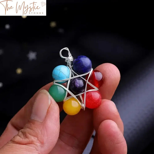 A close-up image of a hexagram star pendant amulet crafted from wire, featuring colorful 7 chakra beads around its edges.