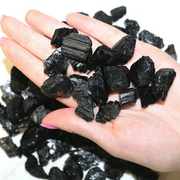 A collection of unpolished, rough black tourmaline stones, varying in size and shape, displayed against a plain background.