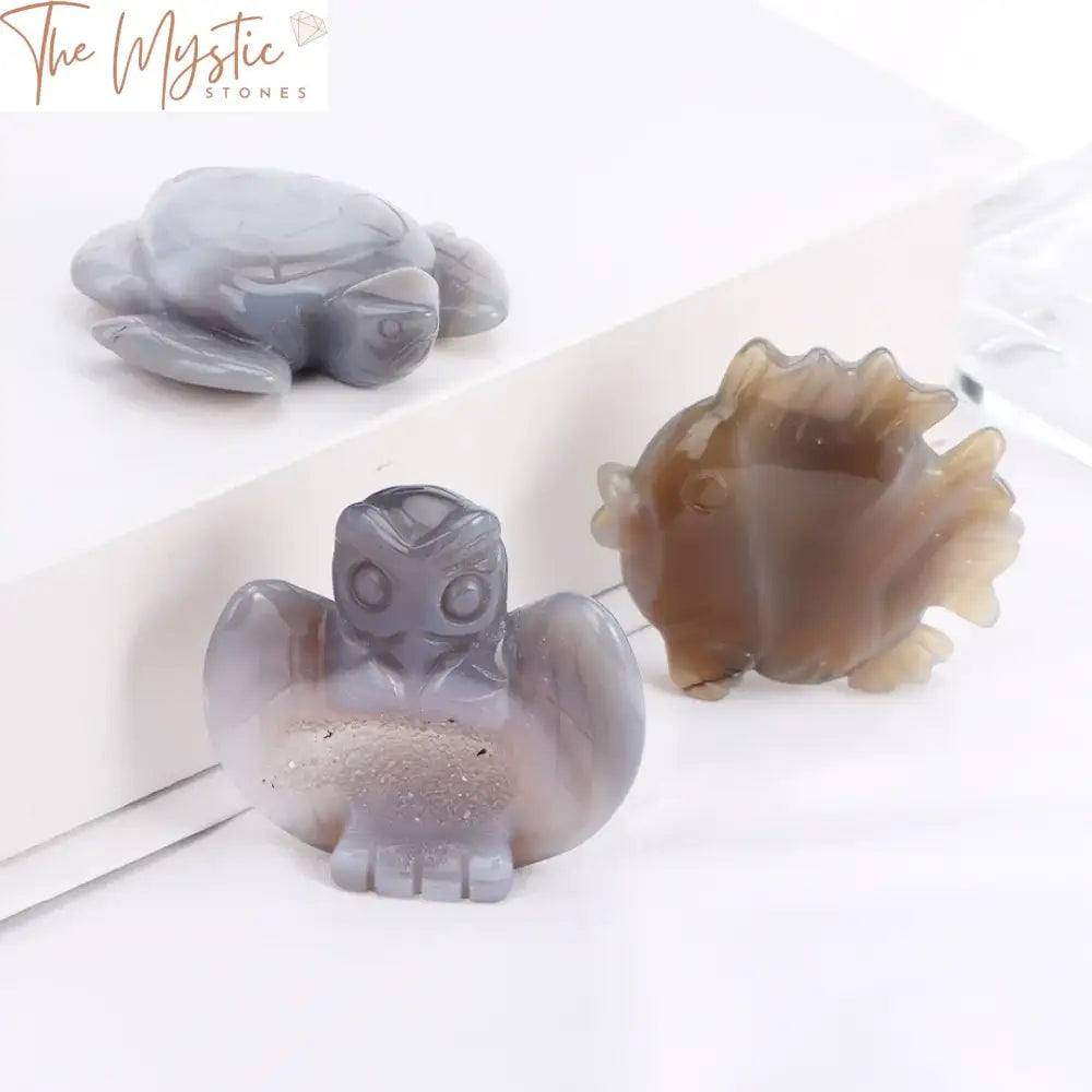 A collection of polished druzy agate stones intricately carved into small statues, including a turtle, fish, and owl.