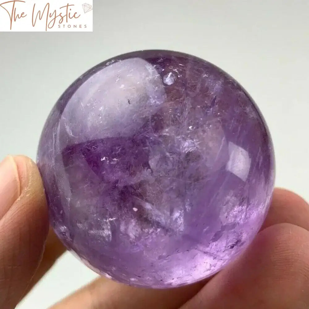 A polished amethyst sphere, deep purple with natural variations and patterns, resting on a small wooden stand.