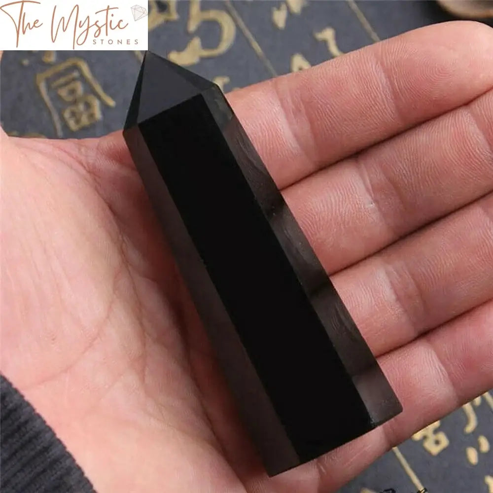 A single hexagonal wand made from black obsidian quartz crystal, with a smooth, glossy surface and sharp, well-defined edges.