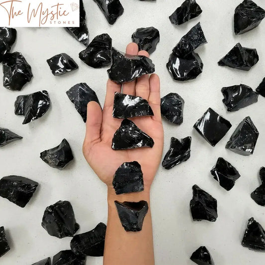 A collection of rough, irregularly shaped black obsidian stones arranged on a light surface.