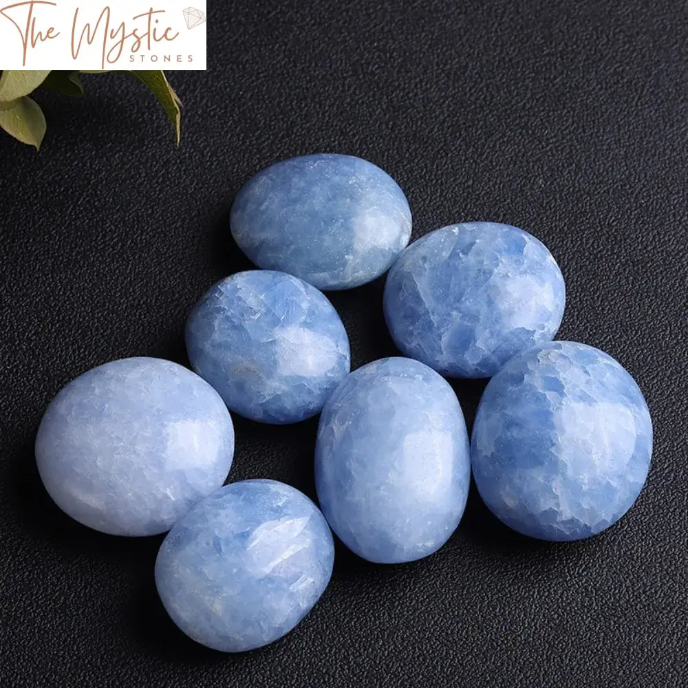 A polished, irregularly shaped blue celestite palm stone rests on a wooden surface.