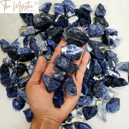 A collection of raw blue sodalite crystals and rough stones are displayed on a wooden surface.