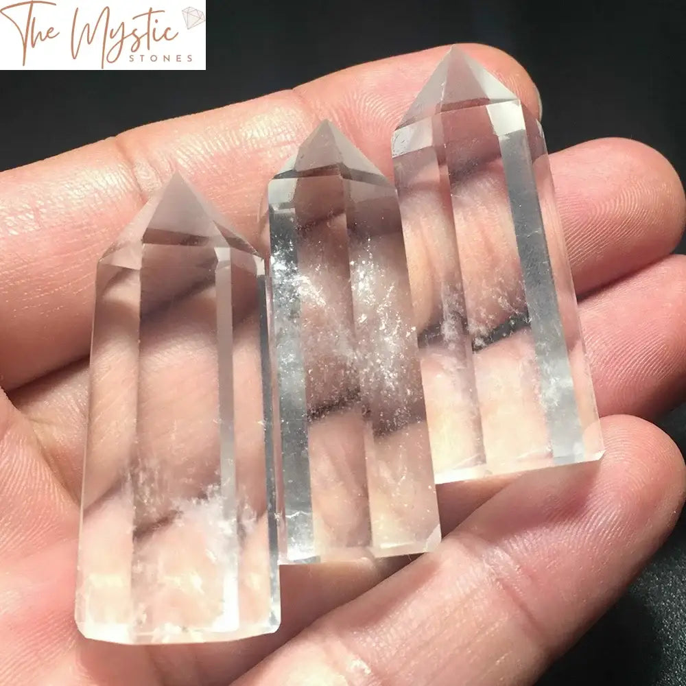 A single clear quartz crystal point, shaped like an obelisk wand, standing upright on a plain surface.