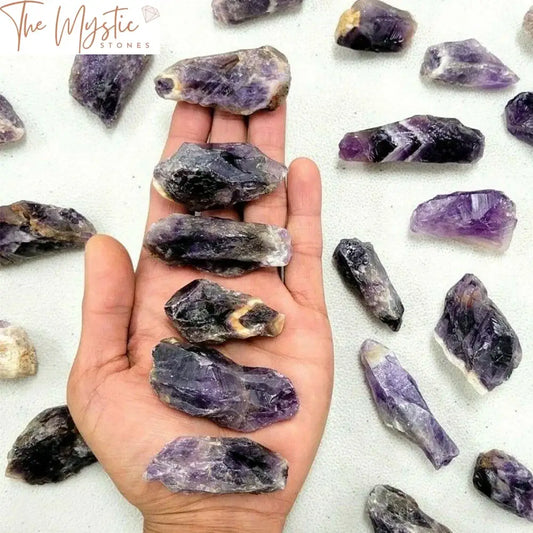 A collection of dark-colored, raw dream amethyst crystals with unique swirling patterns of deep purple and white.