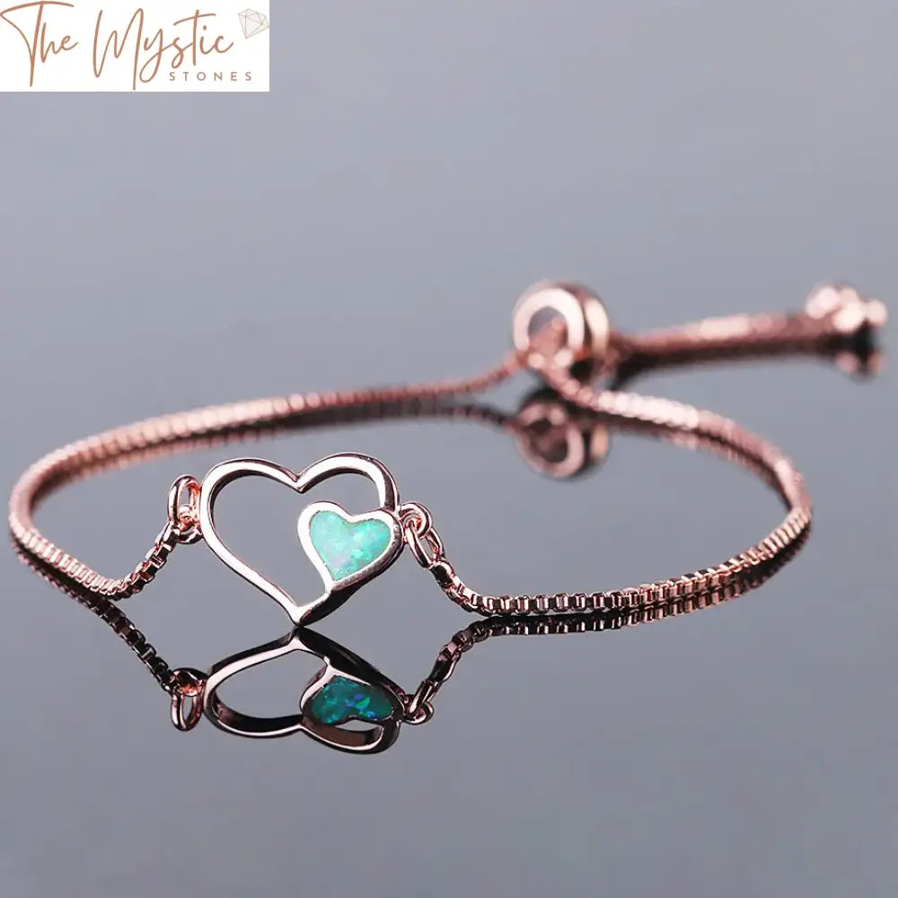 A delicate and elegant bracelet featuring two intertwined heart-shaped settings, each housing a vibrant, fiery opal gemstone.