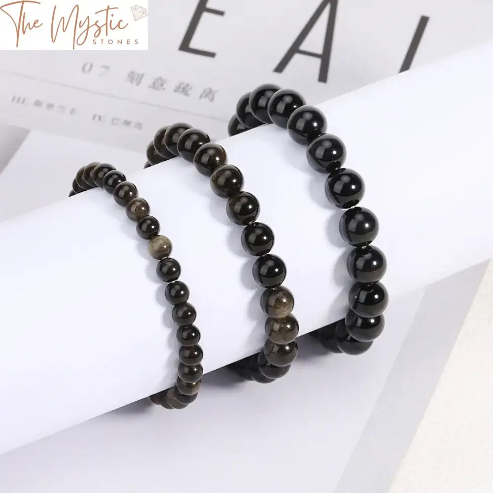 A gold-obsidian bracelet featuring round beads in sizes 6mm, 8mm, and 10mm.