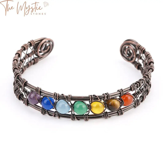 A natural stone 7 chakra bracelet featuring gold-colored wire wrapped copper bangle with an open cuff design.