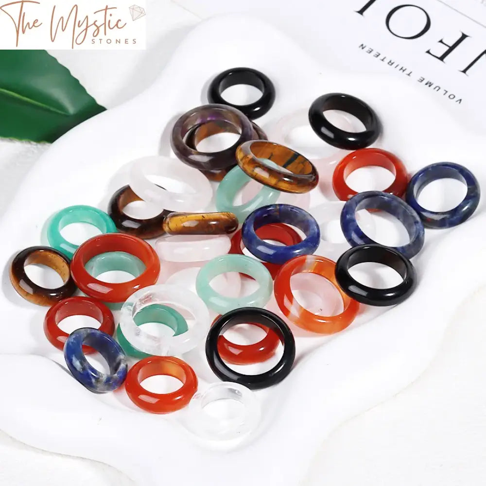 A collection of healing crystal band rings featuring a variety of natural stones, including quartz, red agates, and jaspers.