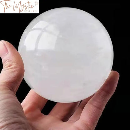 A large 80mm natural white calcite crystal ball resting on a wooden stand, showcasing its clear, translucent appearance.