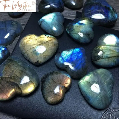 A heart-shaped labradorite crystal with an iridescent play of colors sits on a smooth surface.