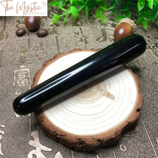 A glossy black obsidian crystal wand, tapered at one end, lies on a smooth white surface.