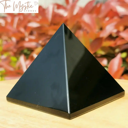 A glossy black obsidian pyramid with a smooth, reflective surface, situated on a light-colored wooden table.