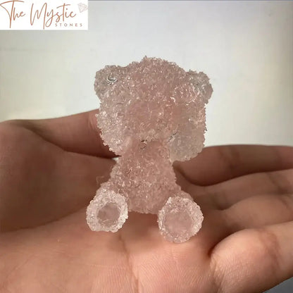 A shiny pink teddy bear figurine made from natural crystal smelting and resin epoxy sits on a sleek surface.