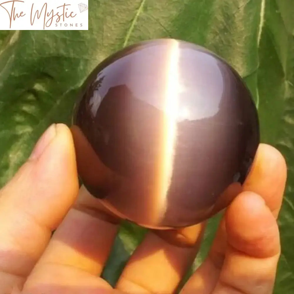 A 40mm rare natural quartz purple cat eye crystal sphere resting on a smooth surface.