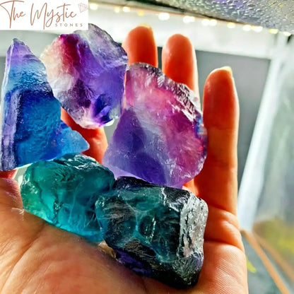 A colorful array of raw, unpolished Rainbow Fluorite crystal stones scattered across a light background.