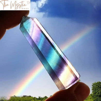 A hexagonal wand made of natural rainbow fluorite quartz crystal with vibrant bands of purple, green, and clear hues.