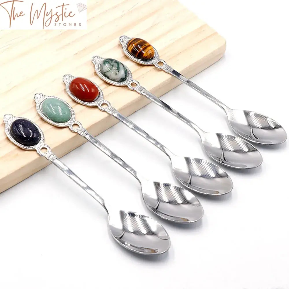 A stainless steel spoon with an elegant, elongated handle is adorned with a polished rose quartz gemstone at the end.