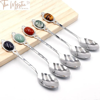 A stainless steel spoon with an elegant, elongated handle is adorned with a polished rose quartz gemstone at the end.