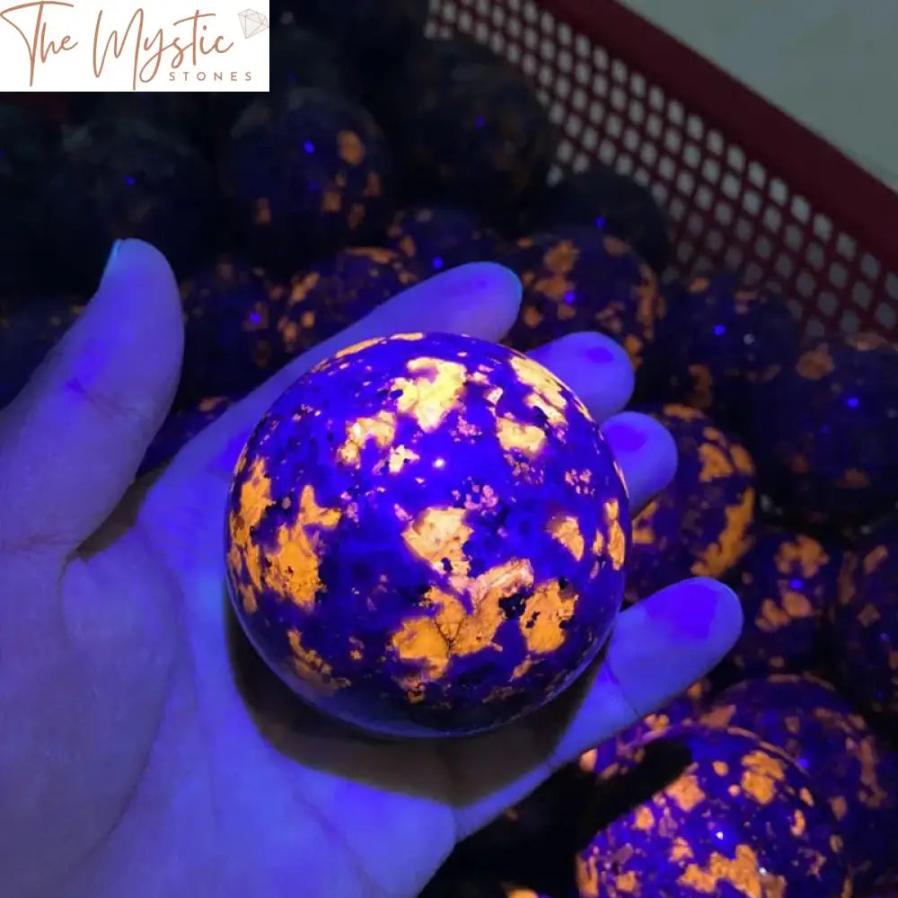 A polished Yooperlite crystal sphere sits on a dark wooden stand.